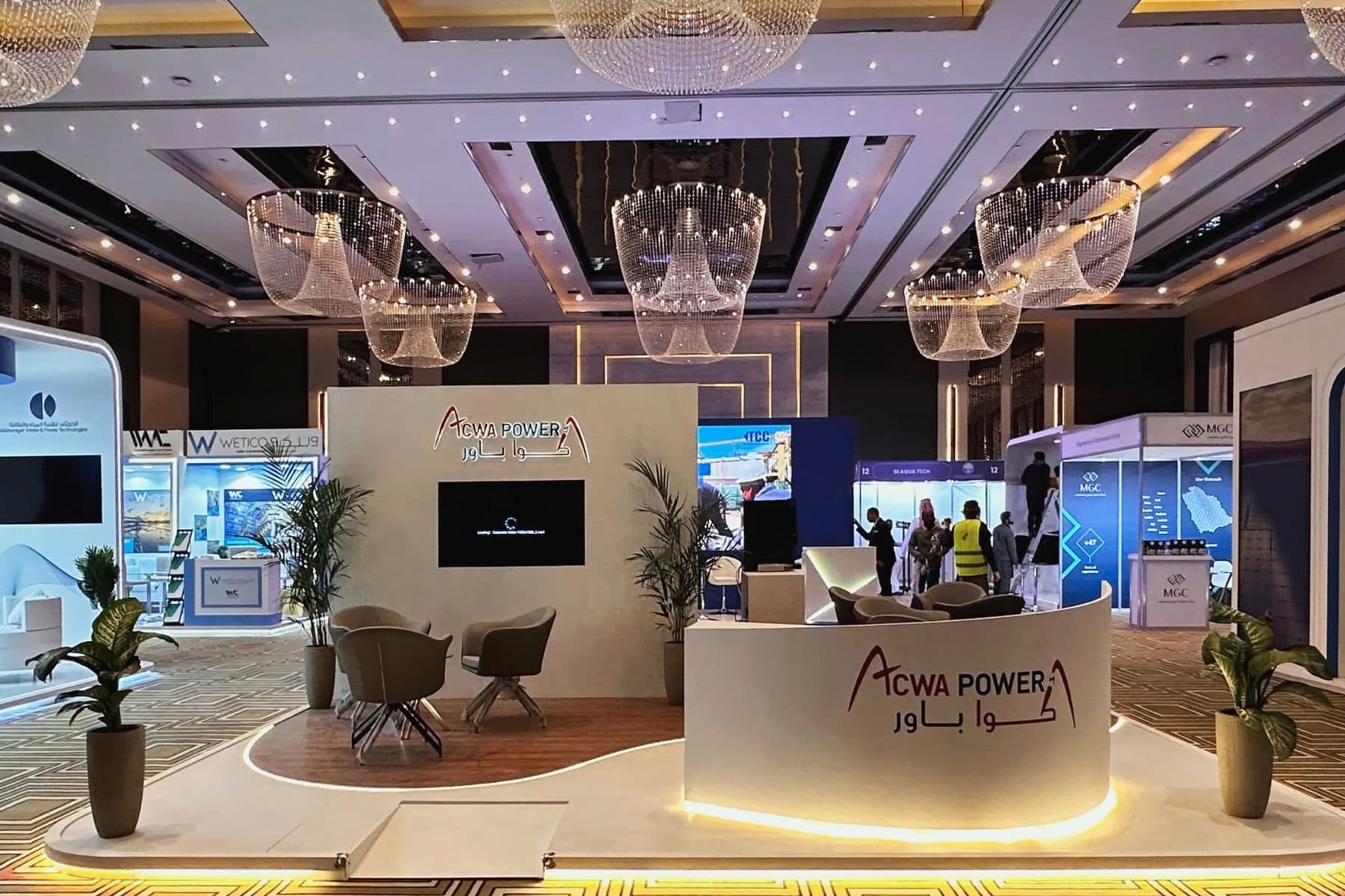 Island exhibition stand built for ACWA Power in a hotel ballroom with an illuminated logo wall and curved reception counter