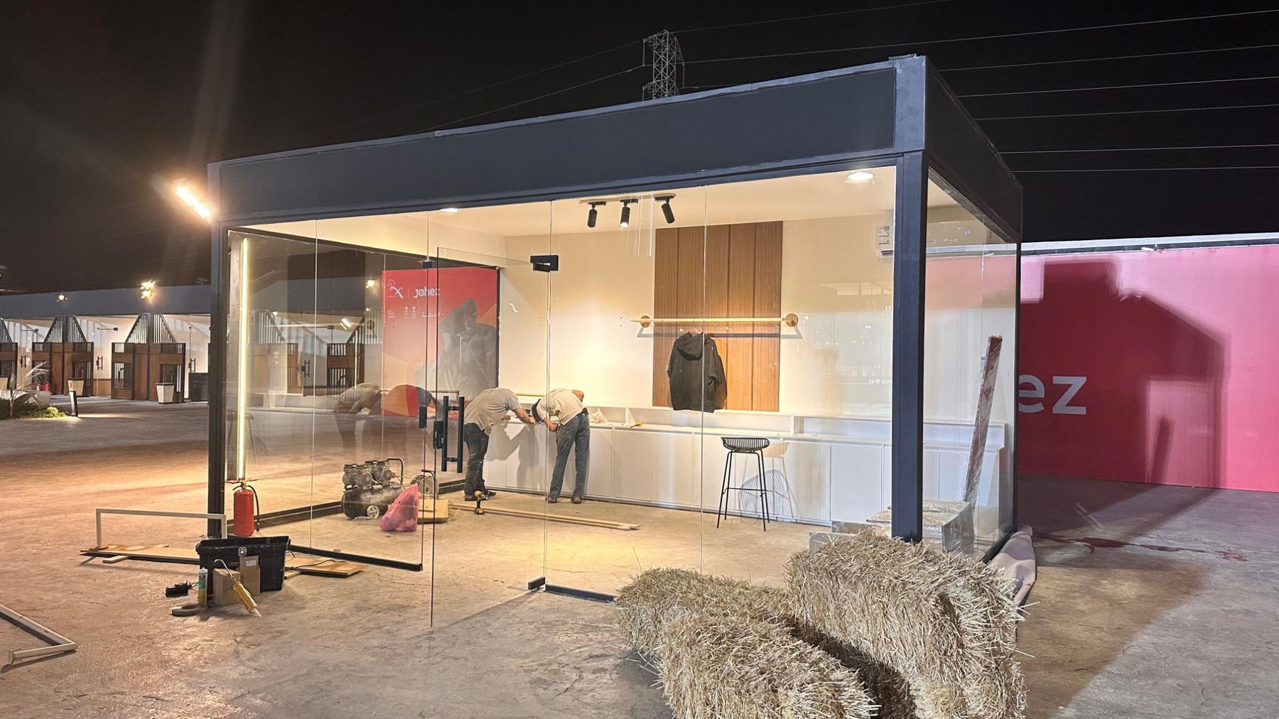 Glass-walled exhibition booth being fitted out on site at night by the Darb crew in Riyadh